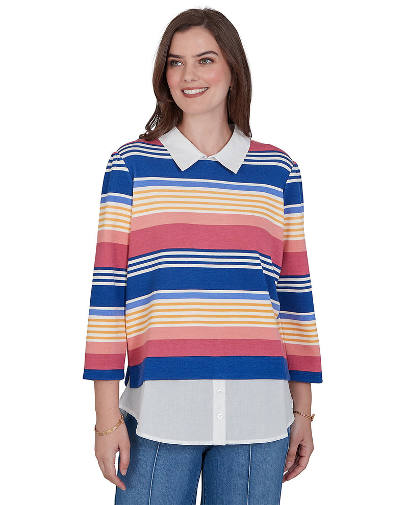 A woman modeling a long-sleeve collared knit top with horizontal stripes in blue, pink, yellow, and white, paired with blue jeans against a plain white background.