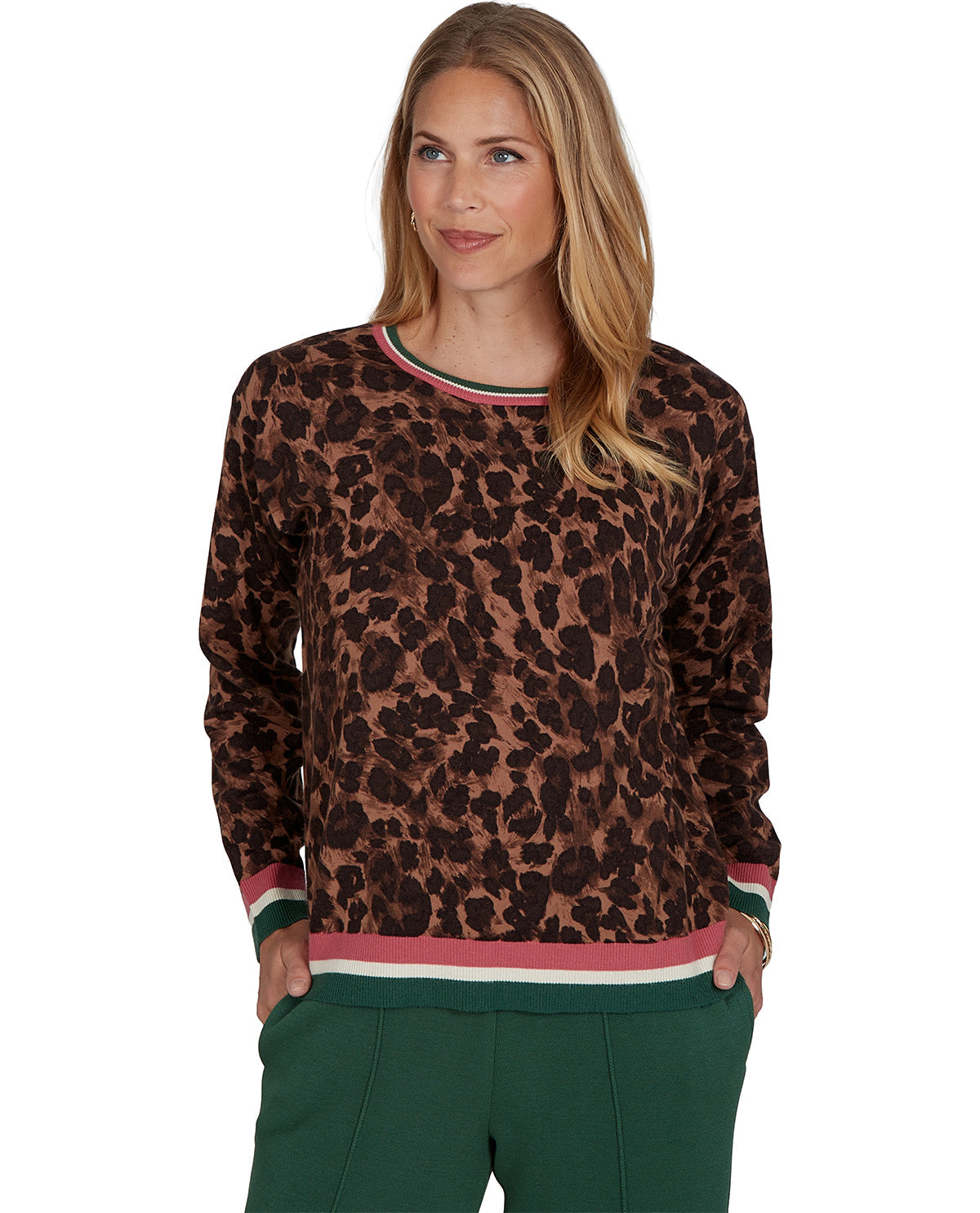 A woman modeling a brown and black leopard print long-sleeve top with green, pink, and white striped ribbed trim at the collar, cuffs, and hem, paired with dark green pants against a plain white background.