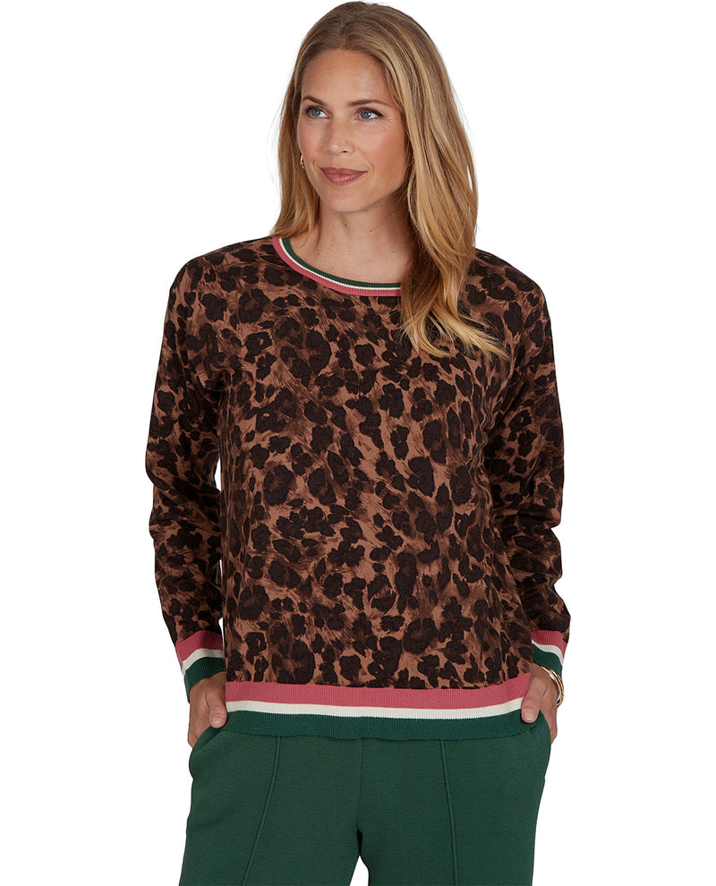 A woman modeling a brown and black leopard print long-sleeve top with green, pink, and white striped ribbed trim at the collar, cuffs, and hem, paired with dark green pants against a plain white background.