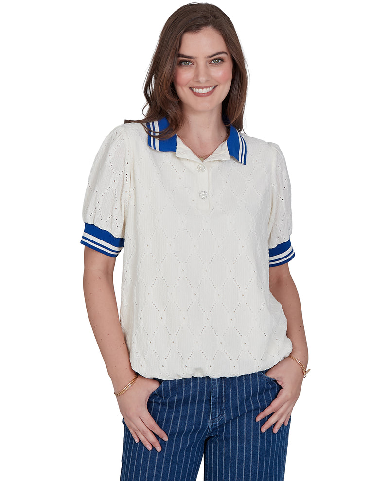 A woman modeling a short-sleeve knit polo shirt in off-white with blue and white striped accents on the collar and cuffs, paired with blue pinstriped pants against a plain white background.