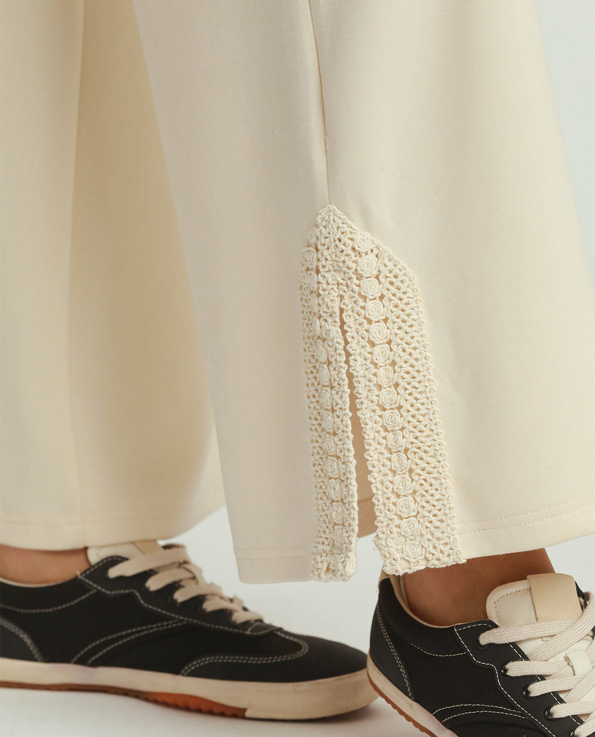 Close-up of black sneakers with white laces worn with beige pants featuring a textured side panel.