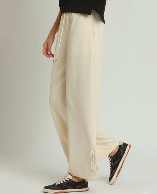 Person wearing beige wide-leg pants and black sneakers on a plain background
