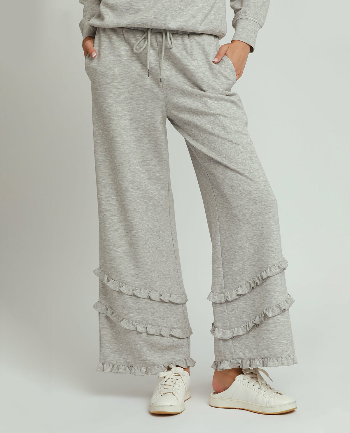 Person wearing gray ruffled pants and a matching top on a white background