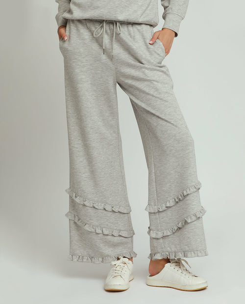 Person wearing gray ruffled pants and a matching top on a white background