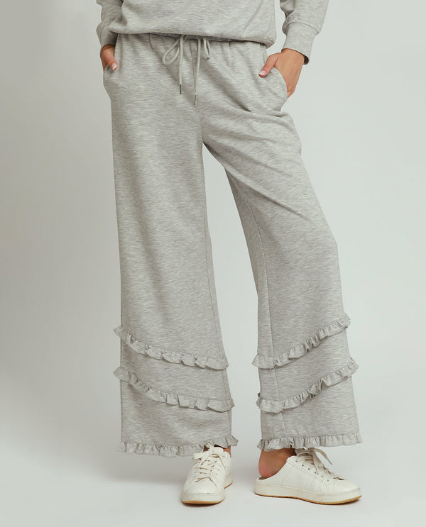 Person wearing gray ruffled pants and a matching top on a white background