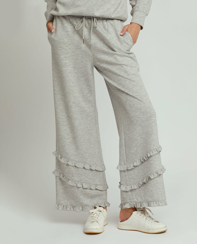 Person wearing gray ruffled pants and a matching top on a white background