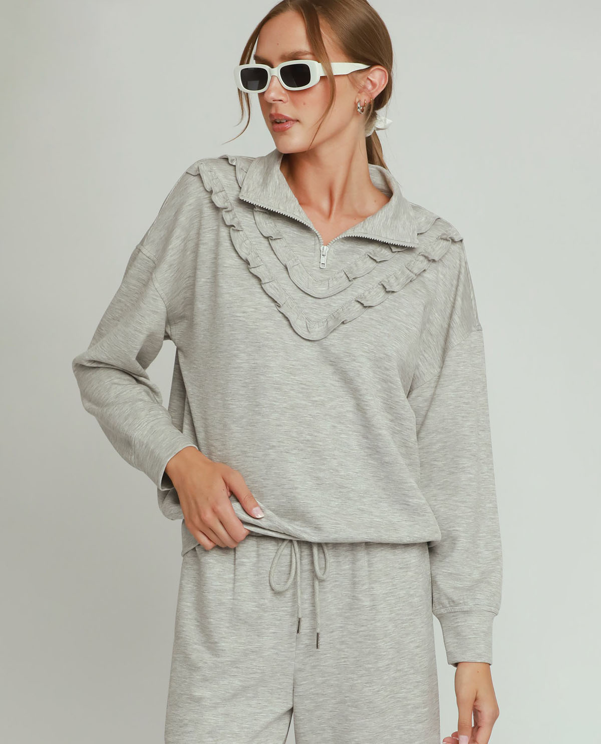 Woman wearing a gray ruffled top and pants on a plain background
