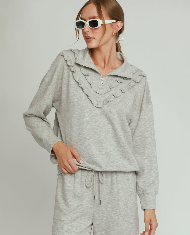 Woman wearing a gray ruffled top and pants on a plain background