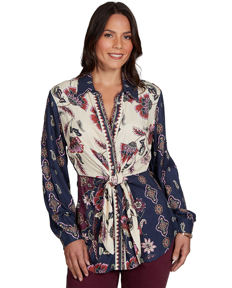 Woman wearing a long-sleeve, patterned shirt with a tie waist on a white background