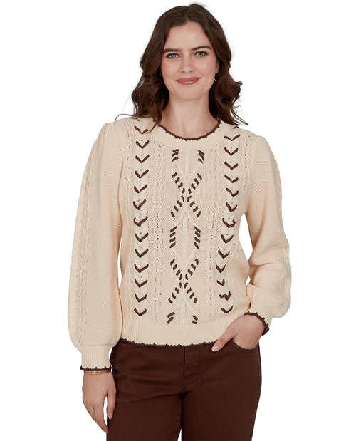 Woman wearing a beige cable knit sweater with intricate patterns on a white background