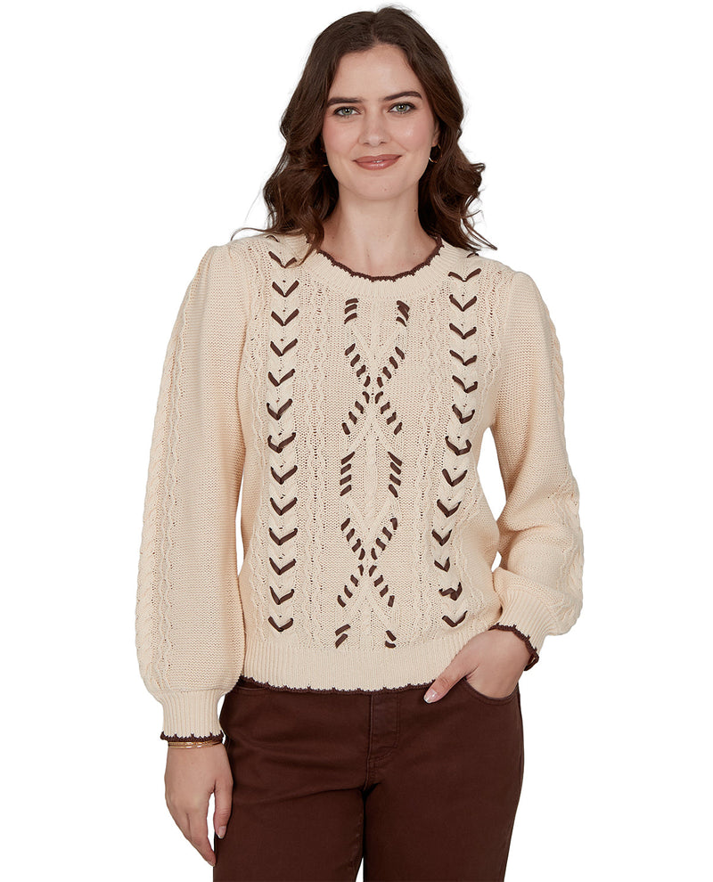 Woman wearing a beige cable knit sweater with intricate patterns on a white background