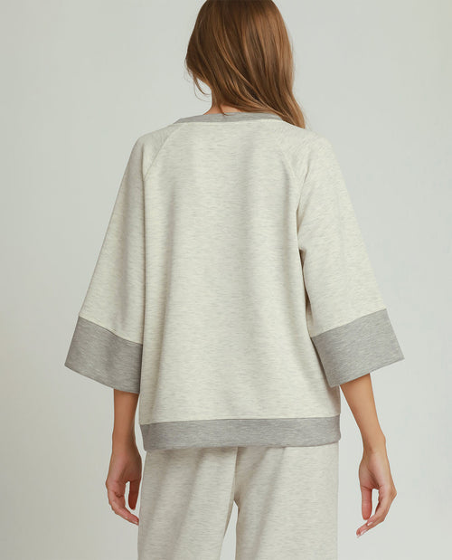 A woman shown from the back wearing a light heather gray sweatshirt with contrasting medium gray ribbed trim at the collar, sleeve cuffs, and hem, paired with matching light heather gray sweatpants, against a light gray studio background.