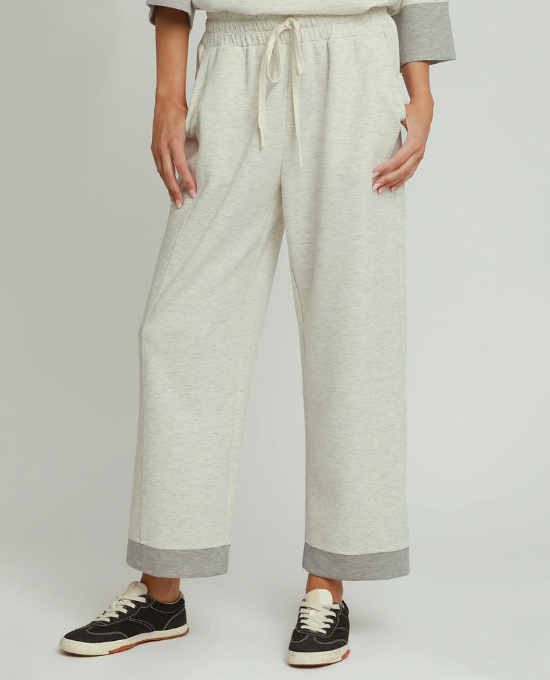 A person wearing light heather gray wide-leg sweatpants with a drawstring waist and contrasting medium gray cuffs, paired with black sneakers, against a light gray studio background.
