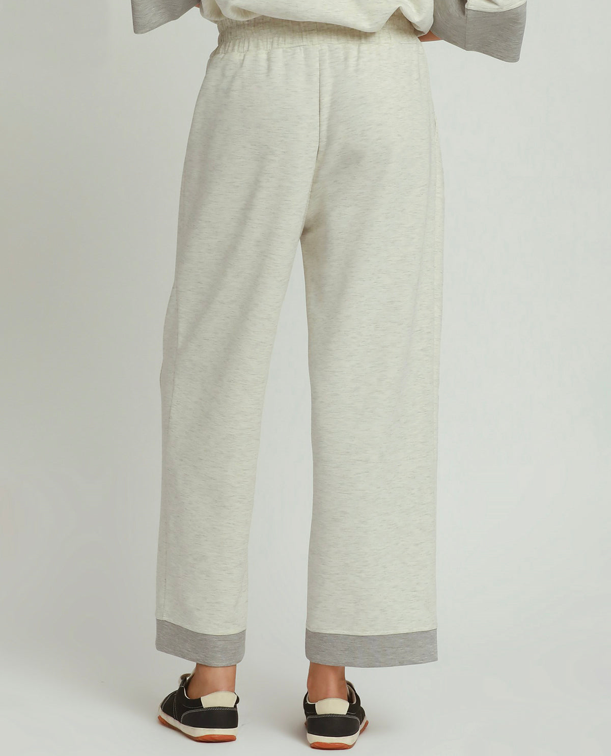 A person shown from the back wearing light heather gray wide-leg sweatpants with contrasting medium gray ribbed cuffs, paired with black slip-on shoes, against a light gray studio background.