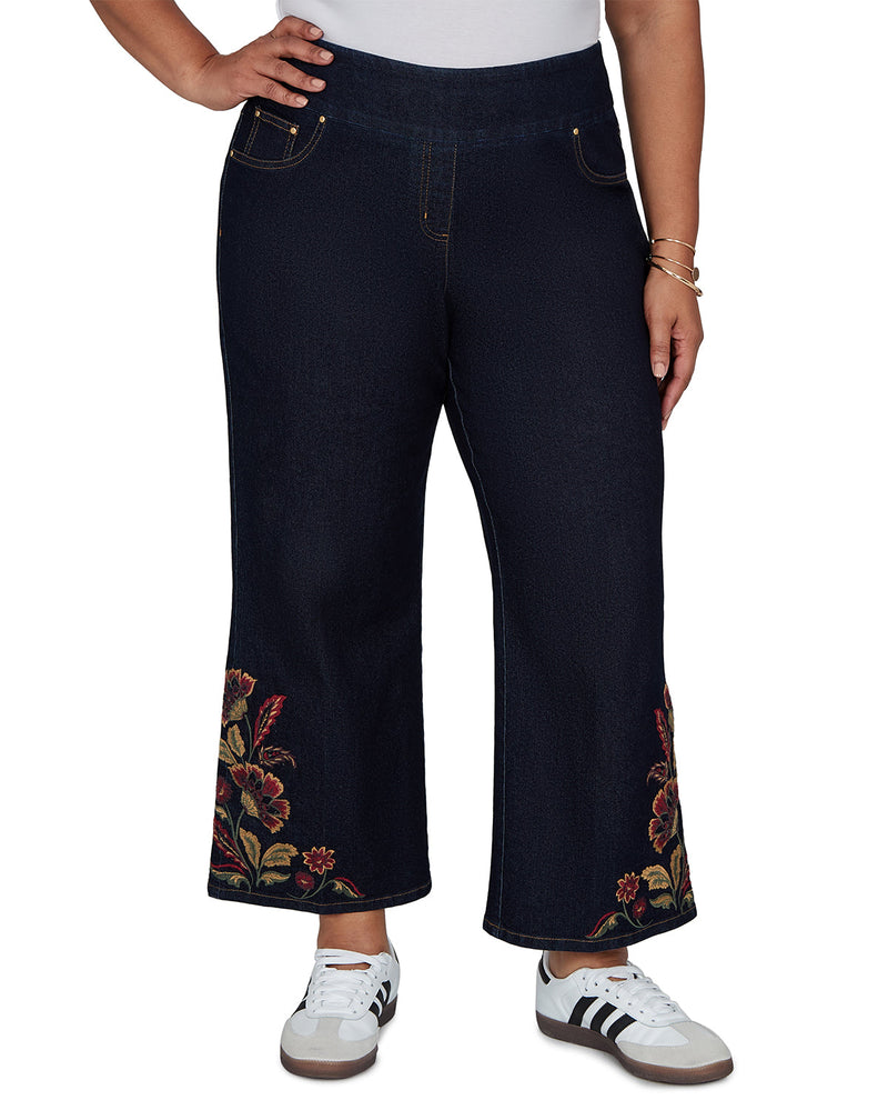 A person wearing dark navy wide-leg cropped jeans with floral embroidery near the hem, paired with white sneakers against a plain white background.