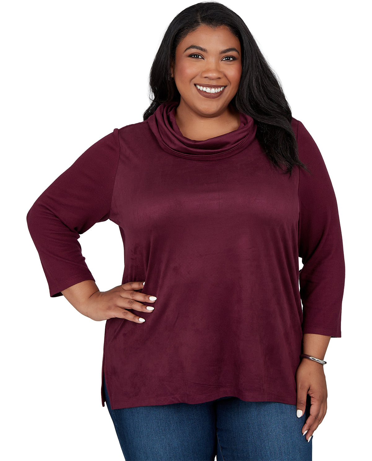 A smiling woman with long black hair wearing a three-quarter sleeve cowl neck top in burgundy, paired with blue jeans, against a plain white background.