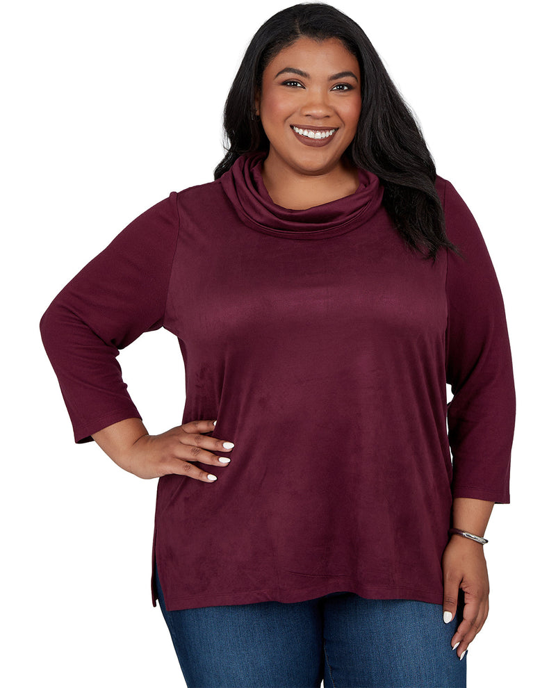 A smiling woman with long black hair wearing a three-quarter sleeve cowl neck top in burgundy, paired with blue jeans, against a plain white background.