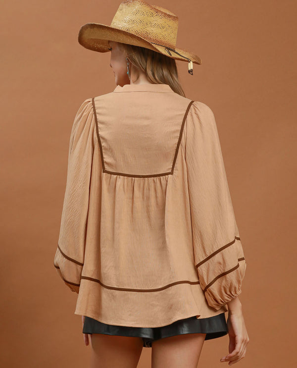 Woman wearing a beige blouse with black trim and a straw hat on a brown background