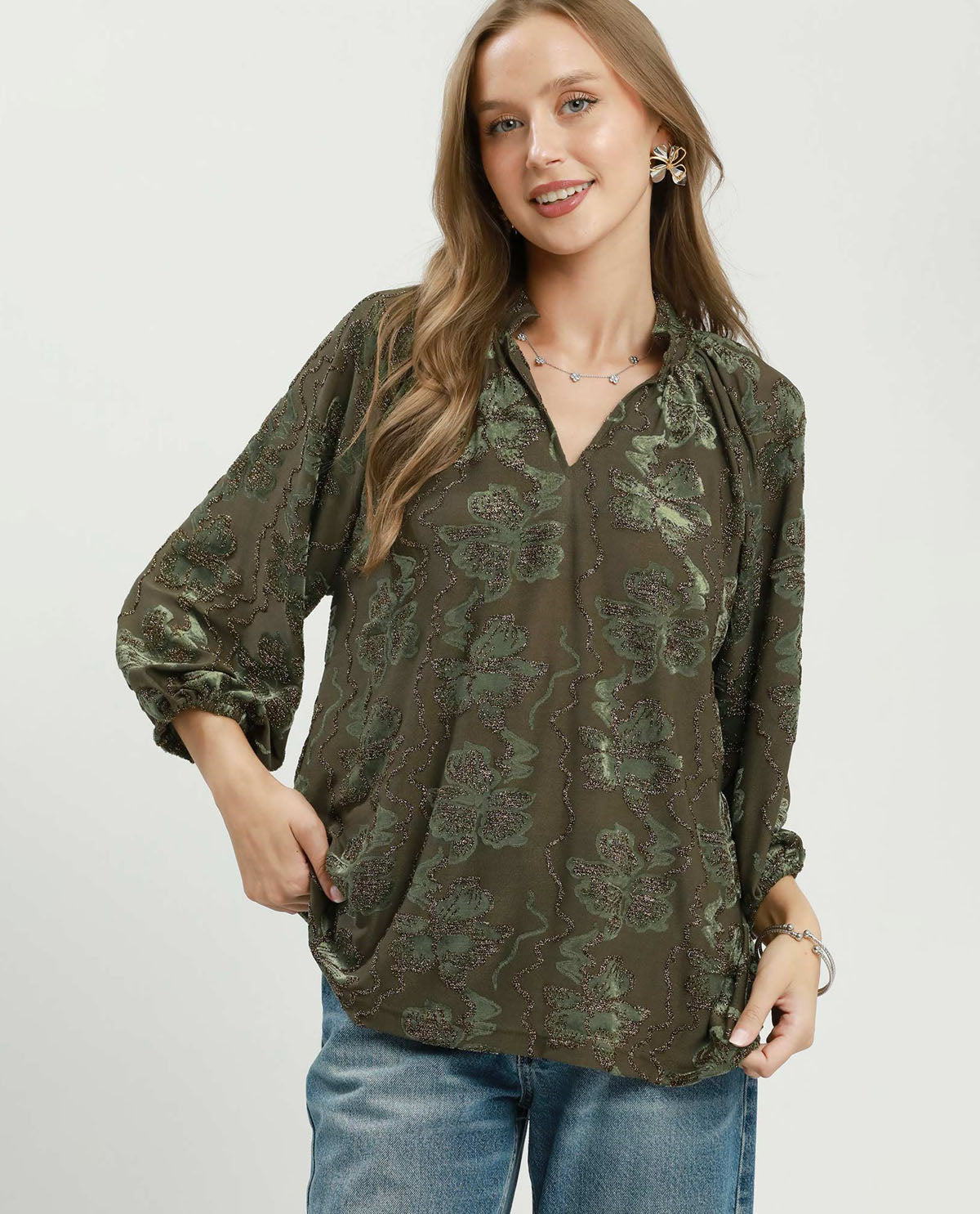 Woman wearing a green floral blouse and blue jeans on a white background