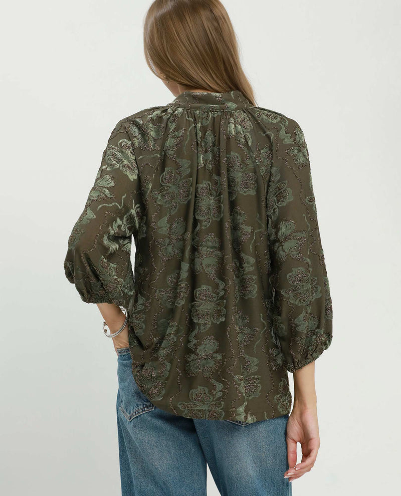 Person wearing a green patterned blouse and blue jeans on a white background