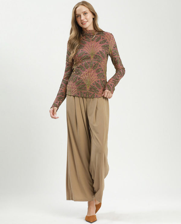 Woman wearing a patterned long-sleeve top and beige wide-leg pants on a white background