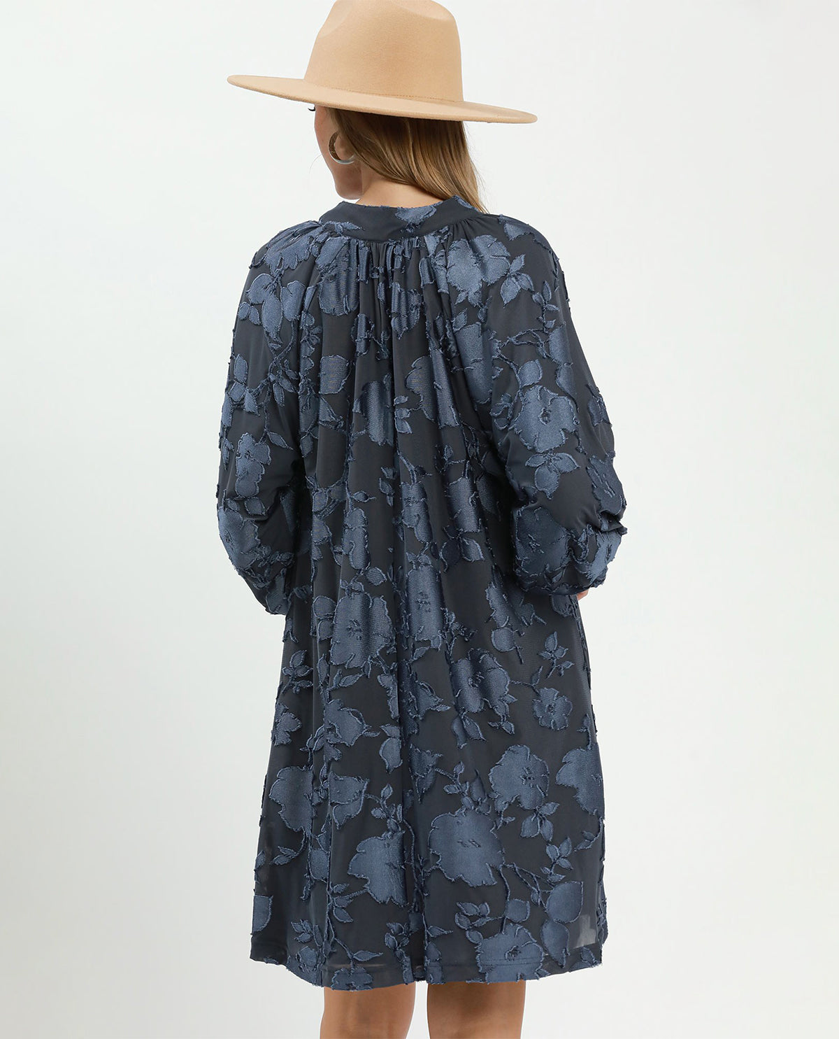 Person wearing a blue floral dress and beige hat on a white background