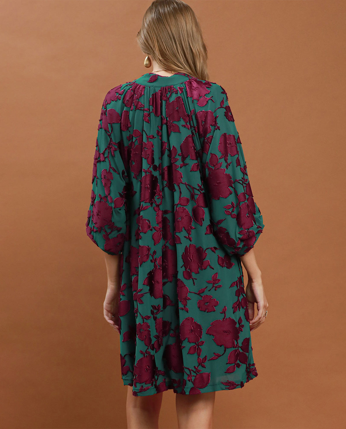 Woman wearing a green and red floral dress against a brown background
