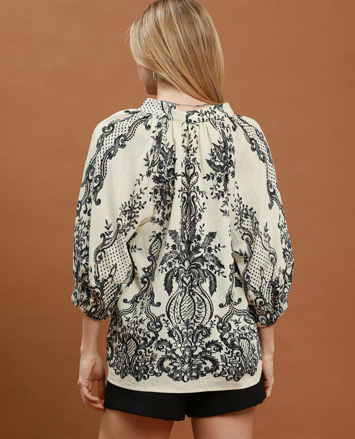 Woman wearing a black and white patterned blouse against a brown background