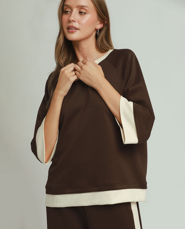 Woman wearing a brown and beige top against a plain background