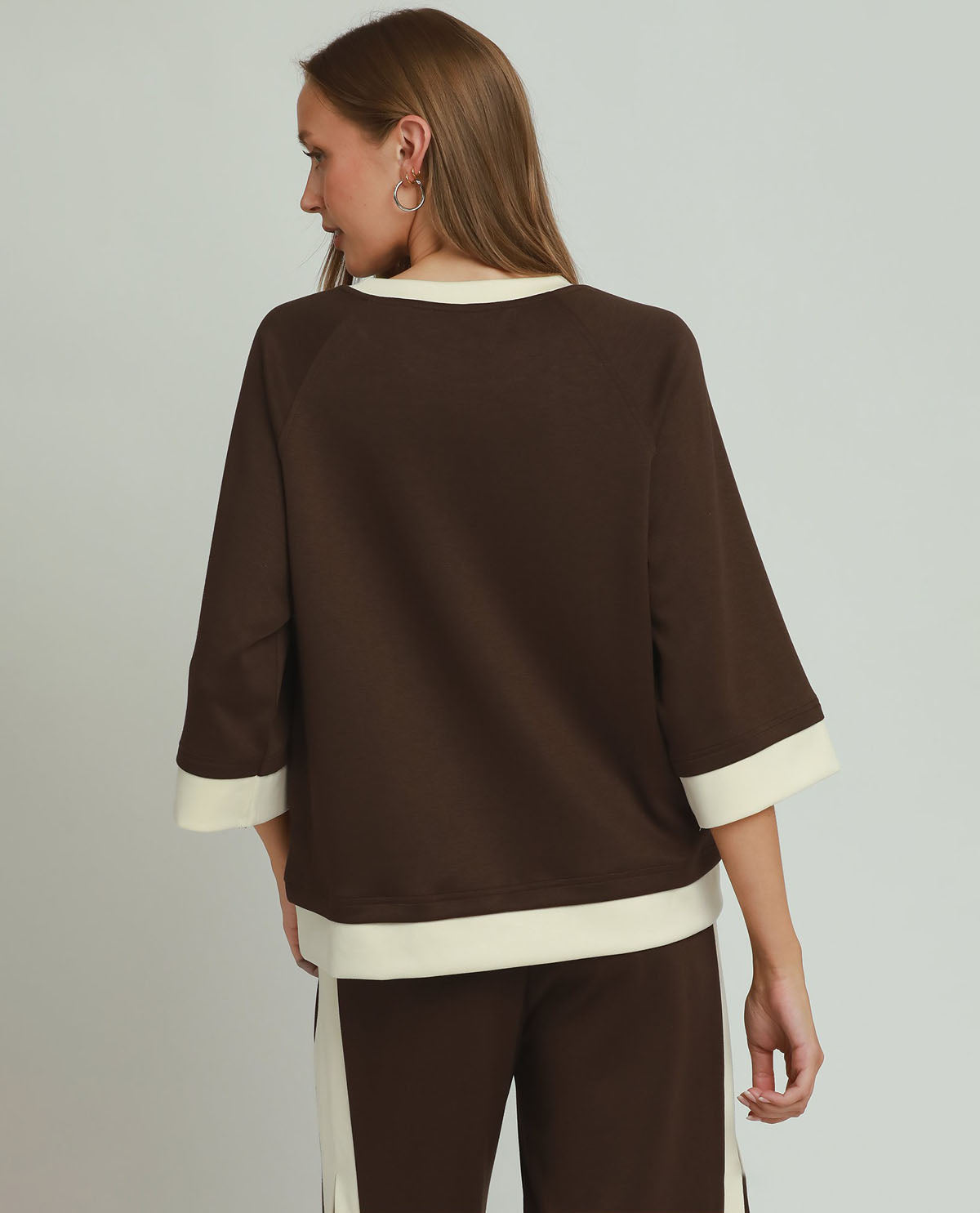 Woman wearing a brown outfit with white accents on a plain background