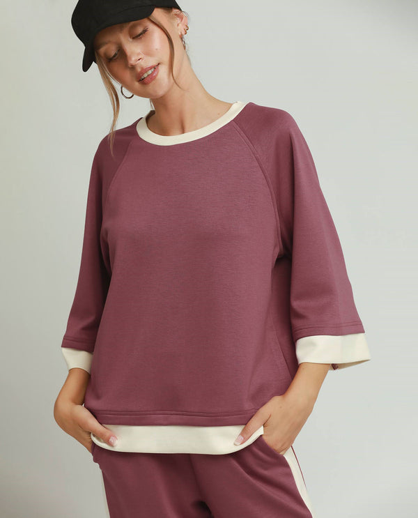 Woman wearing a maroon sweater with white trim on a plain background