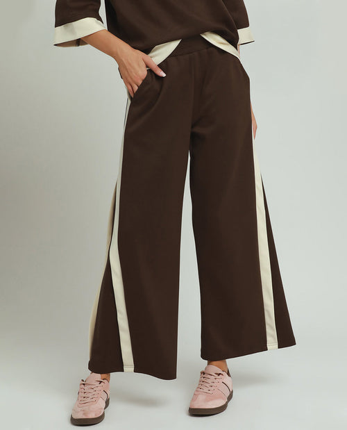 Brown wide-leg pants with white stripes worn by a person on a light gray background