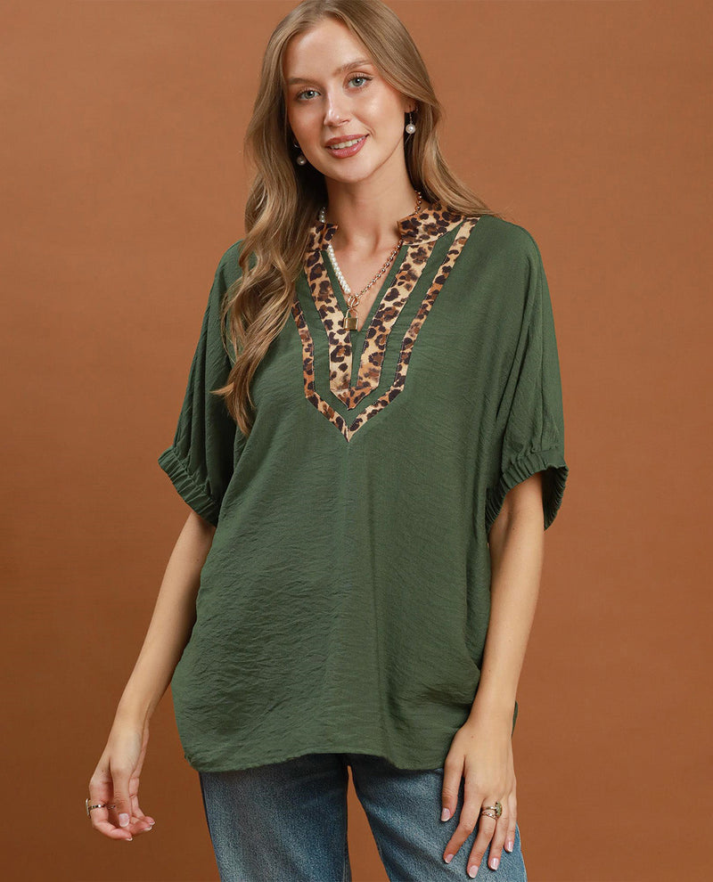 Woman wearing a green top with leopard print details against a brown background