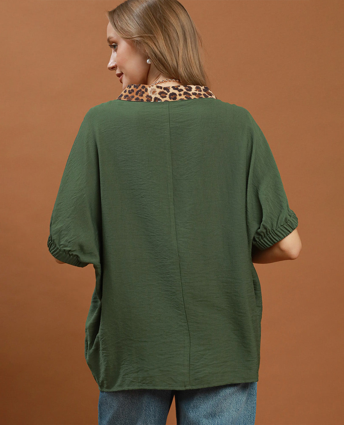Woman wearing a green blouse with a leopard print collar against a brown background