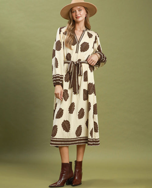 Woman wearing a patterned dress with a beige hat and brown boots on a green background