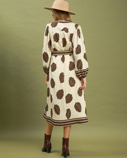 Woman wearing a patterned dress with a beige hat and brown boots on a green background