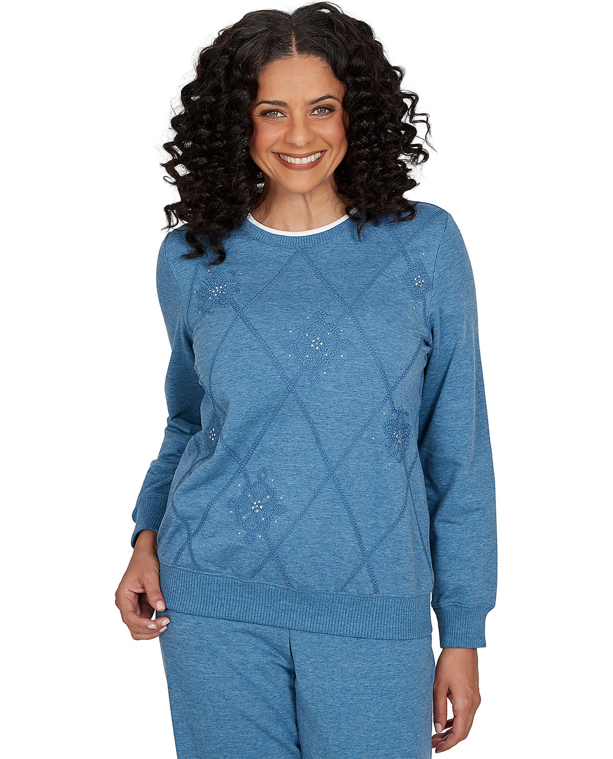 A smiling woman with curly dark hair wearing a heathered blue long-sleeve sweater with a diamond knit pattern and matching blue pants, photographed against a plain white background.