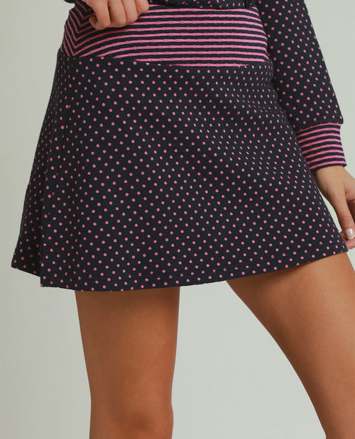 Person wearing a black skirt with pink polka dots and a matching top on a plain background