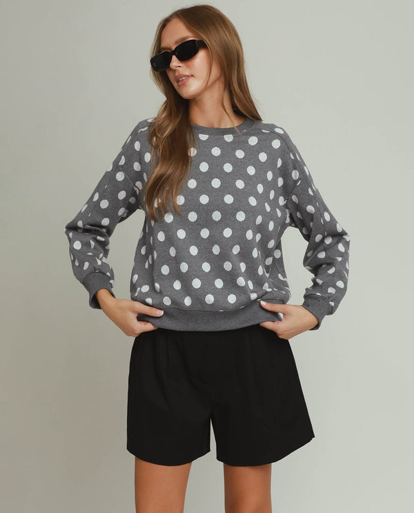 Woman wearing a gray sweater with white polka dots and black shorts against a plain background