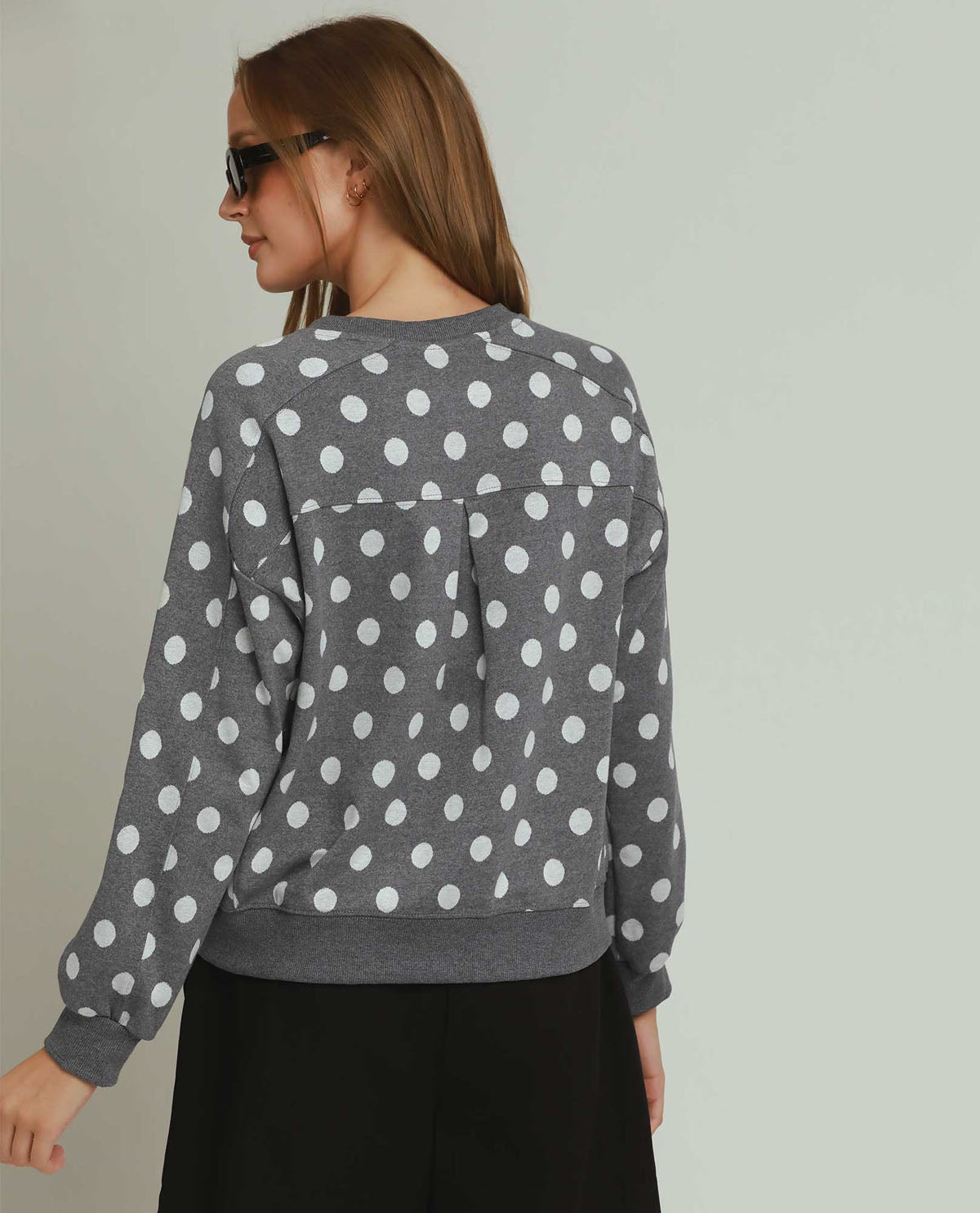 Woman wearing a gray sweater with white polka dots against a plain background