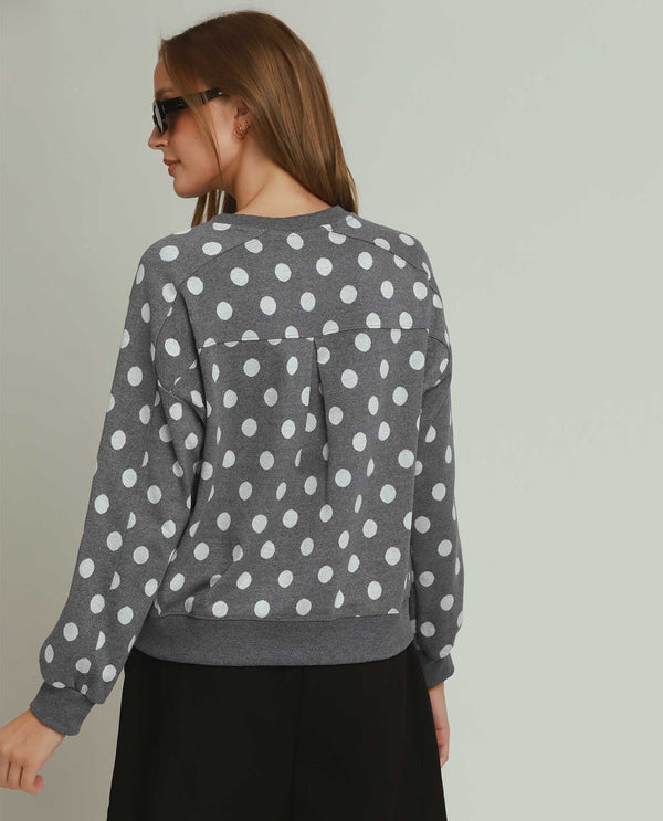 Woman wearing a gray sweater with white polka dots against a plain background