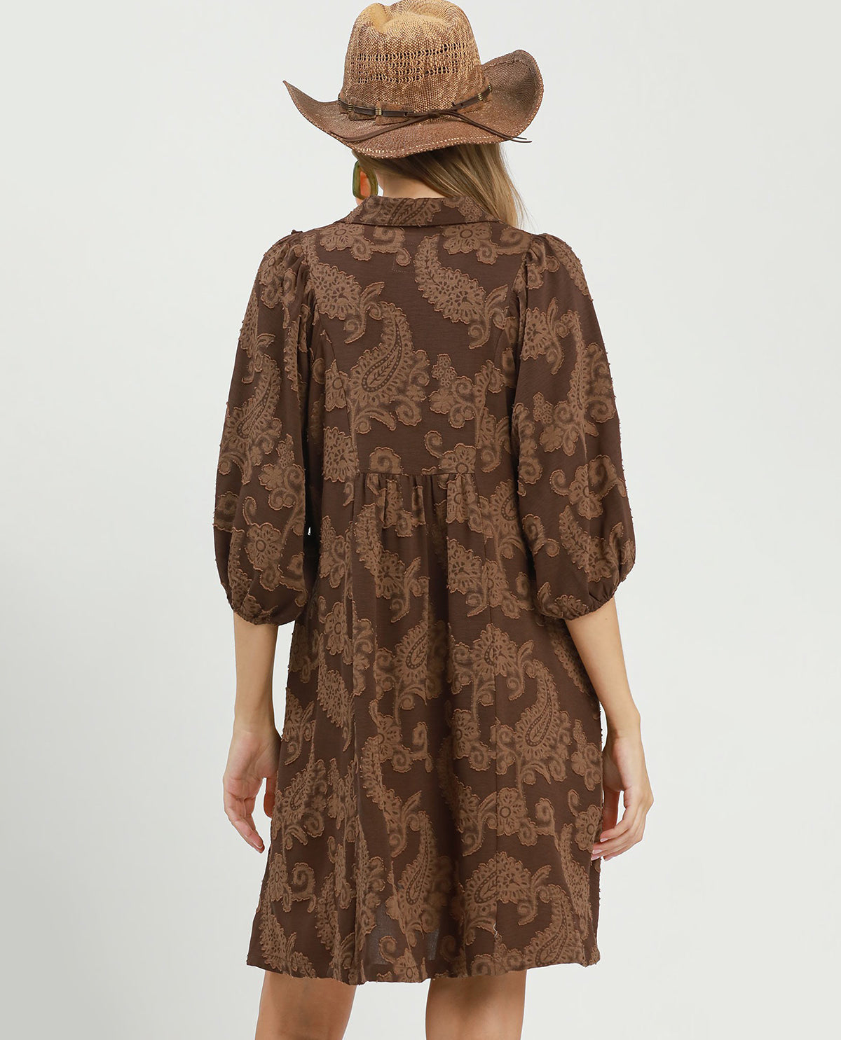 Person wearing a brown patterned dress and hat on a white background