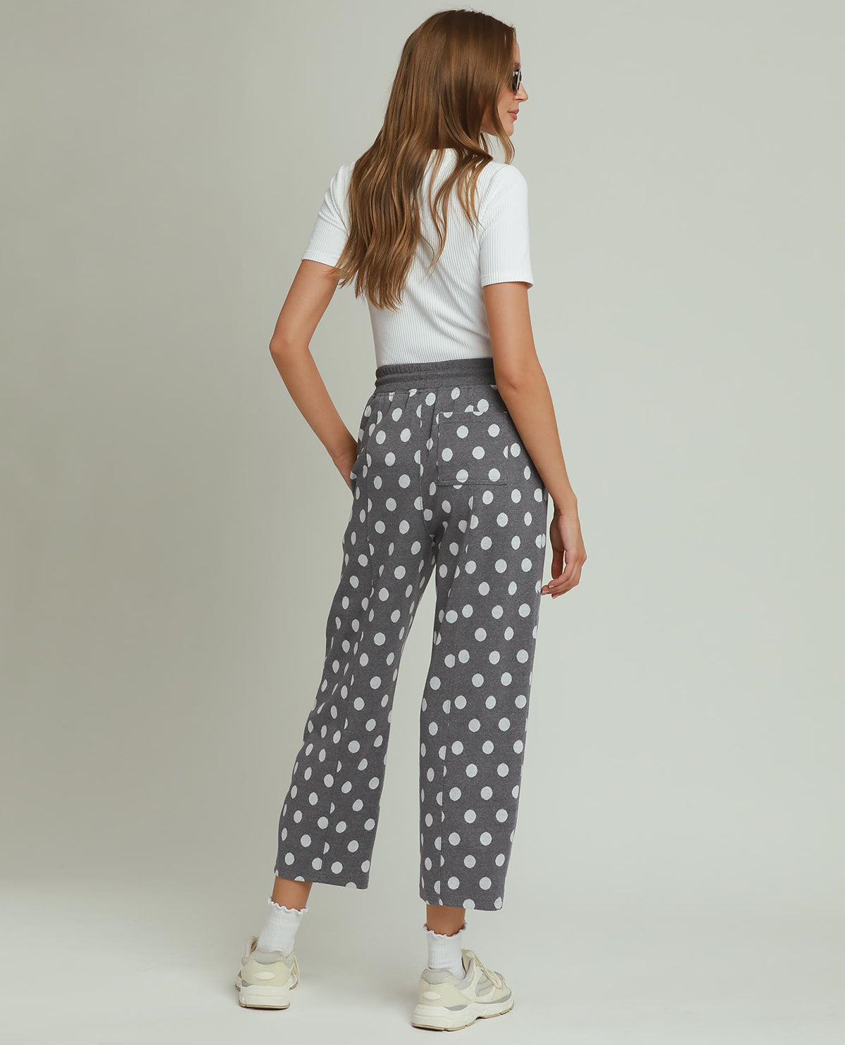 Woman wearing gray polka dot pants and a white top on a plain background