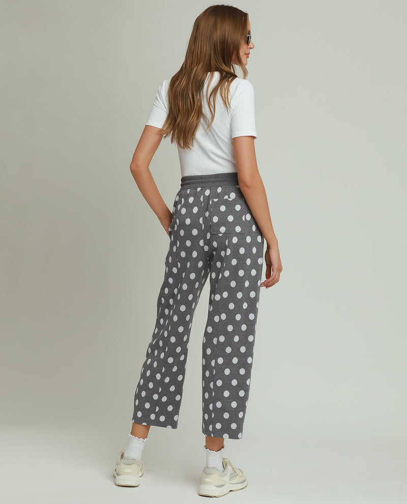 Woman wearing gray polka dot pants and a white top on a plain background
