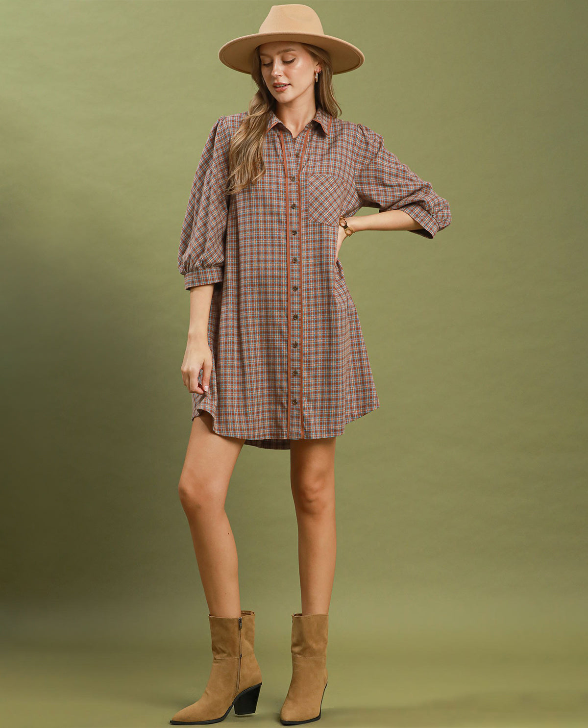 Woman wearing a plaid dress, hat, and boots on a green background