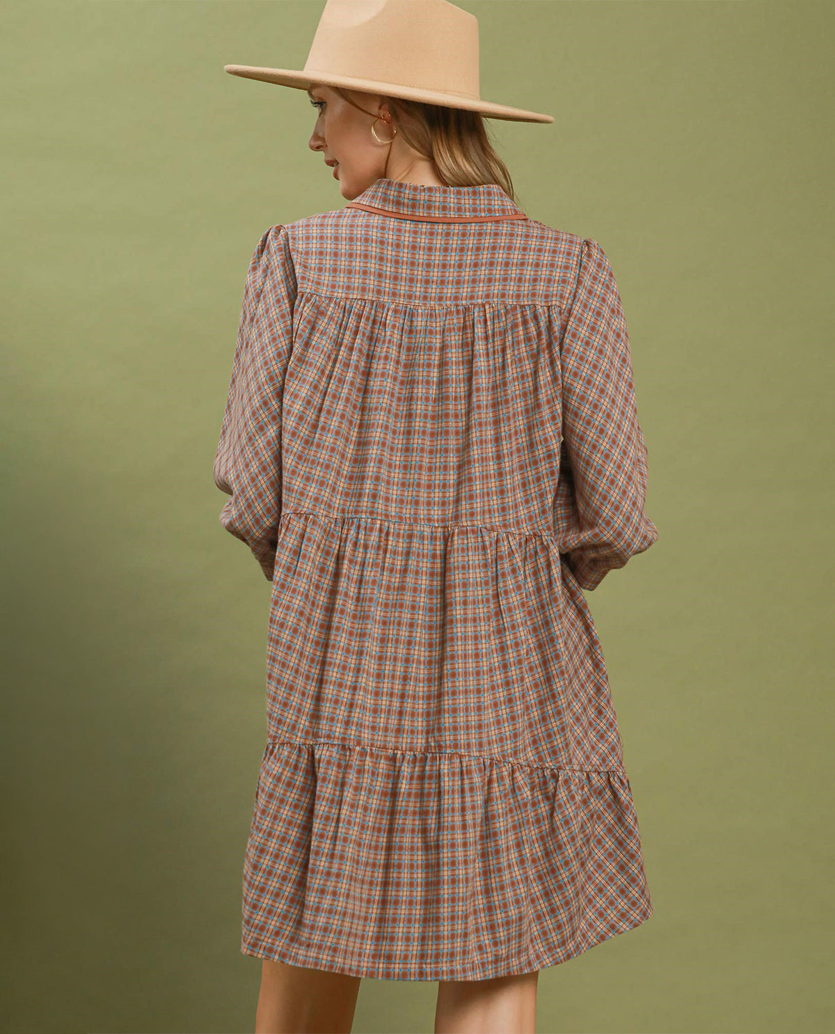 Woman wearing a plaid dress and beige hat against a green background