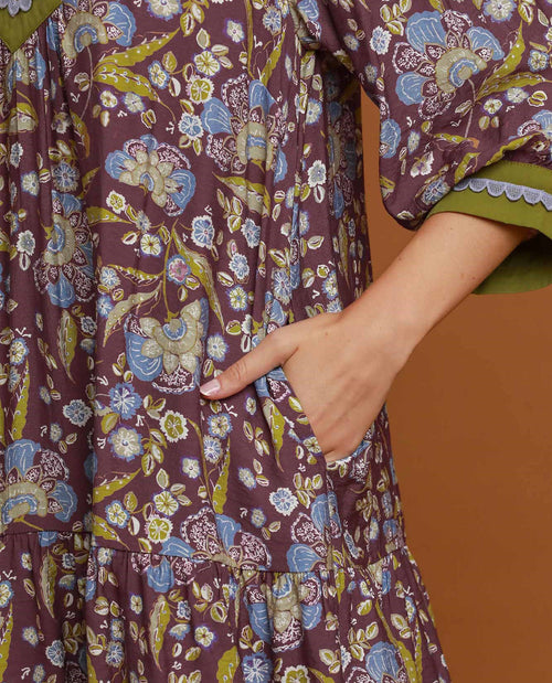 Close-up of a tiered bohemian-style dress with a purple, blue, and olive green floral print, featuring a side pocket and a hand tucked inside.