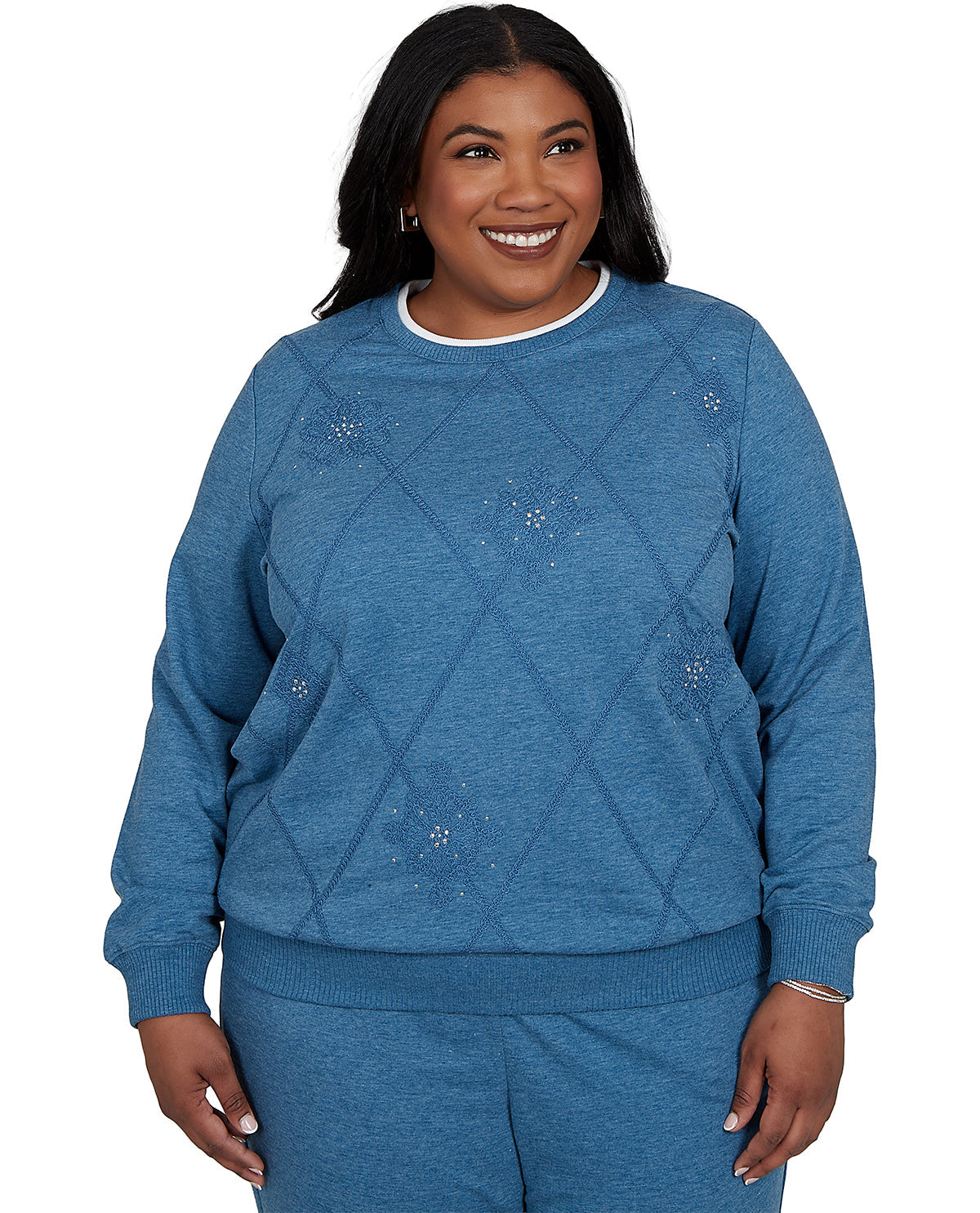 A smiling woman wearing a heathered blue crewneck sweatshirt with a diamond argyle pattern and small rhinestone accents, paired with matching blue sweatpants, against a plain white background.