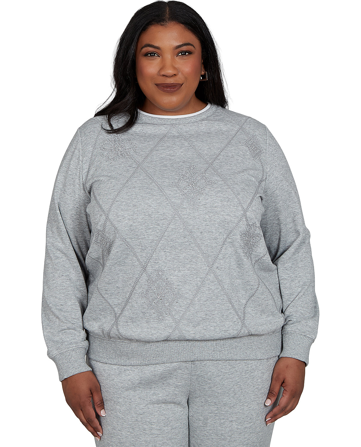 A woman modeling a light gray heather crewneck sweatshirt with a subtle diamond pattern on the front, paired with matching gray sweatpants, against a plain white background.