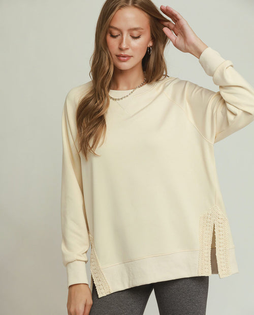 Woman wearing a light-colored sweater with lace details on a plain background